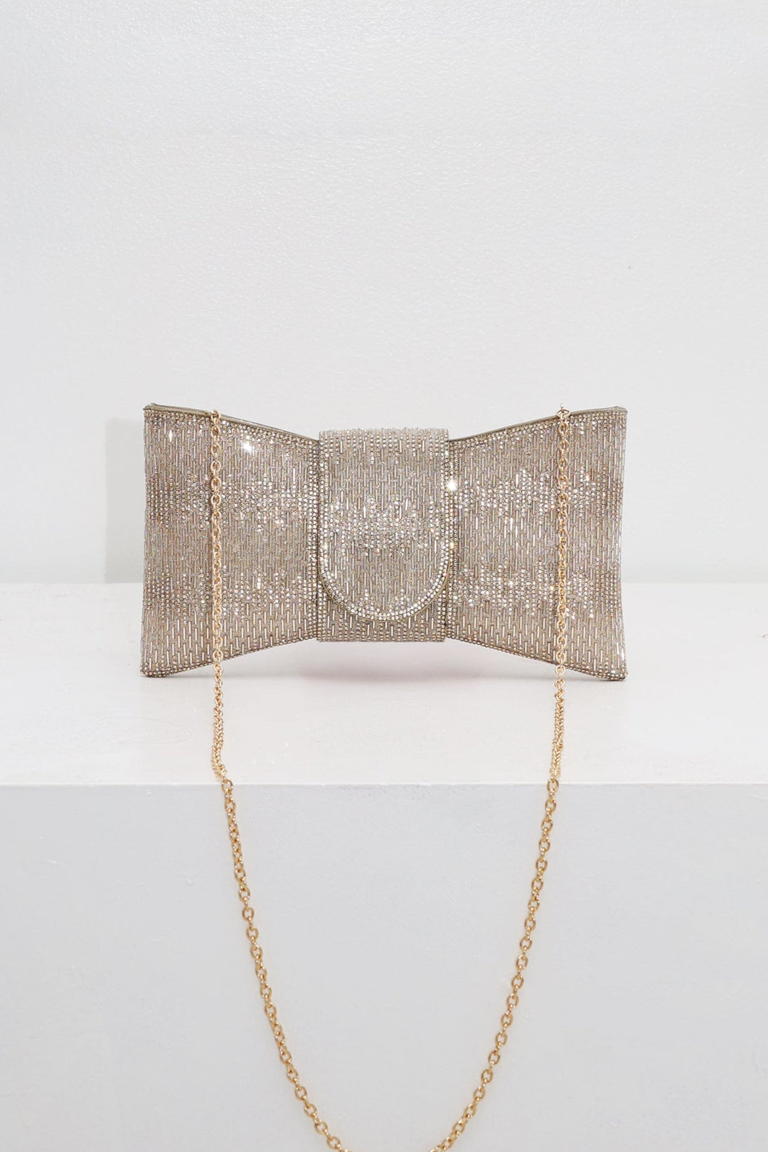EDGE — gold rhinestone bow-shaped evening clutch with chain strap, flat lay