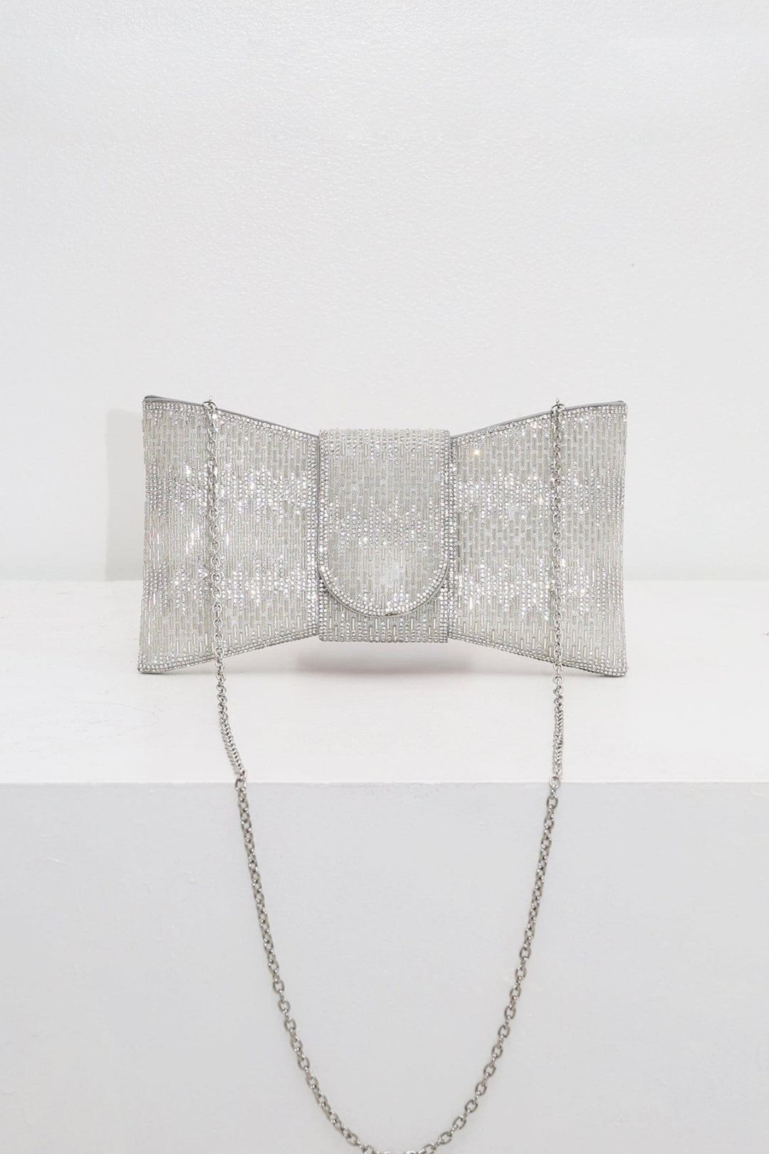 EDGE — silver rhinestone bow-shaped evening clutch with chain strap, flat lay