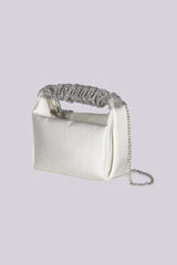 EDGE — ivory satin clutch with a crystal-embellished handle and chain strap, three-quarter side view flat lay