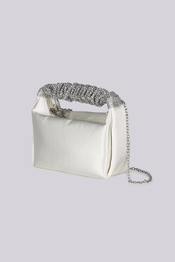 EDGE — ivory satin clutch with a crystal-embellished handle and chain strap, three-quarter side view flat lay