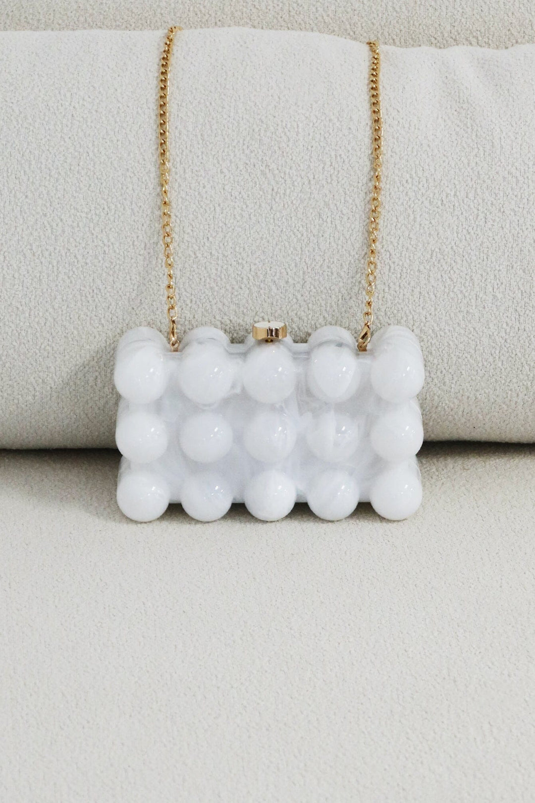 EDGE — pearl bubble-textured mini clutch with gold chain strap draped over a cushion, flat lay