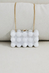 EDGE — pearl bubble-textured mini clutch with gold chain strap draped over a cushion, flat lay