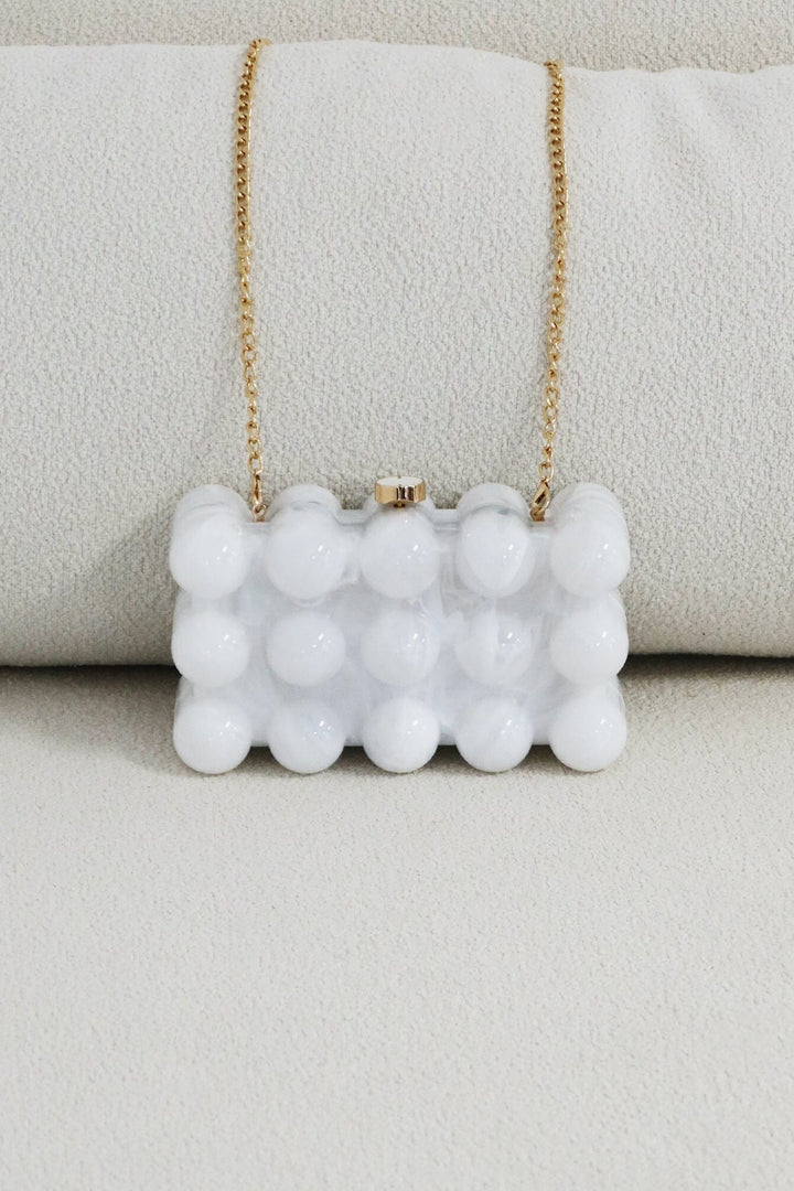 EDGE — pearl bubble-textured mini clutch with gold chain strap draped over a cushion, flat lay