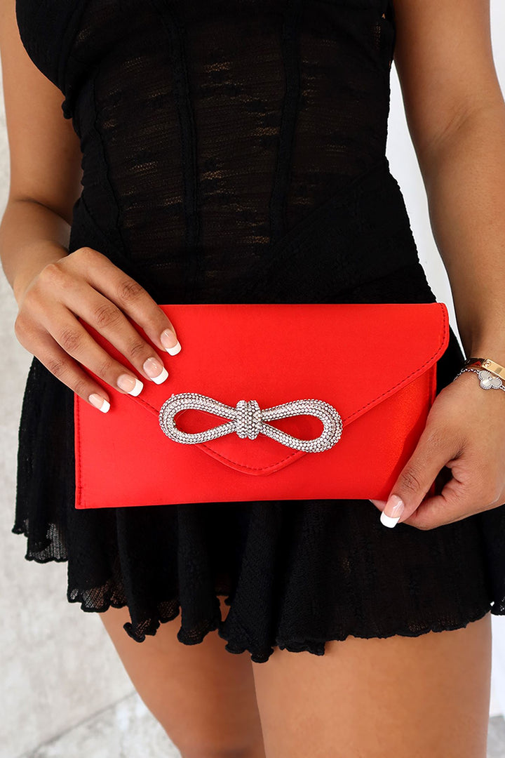 EDGE — red satin clutch with a crystal bow clasp, close-up held by a model
