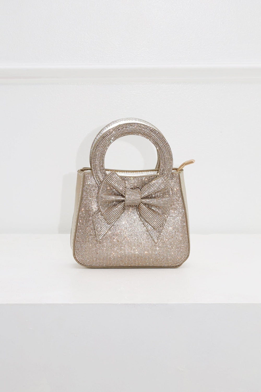 EDGE — gold rhinestone bow-embellished top-handle mini clutch, front view flat lay