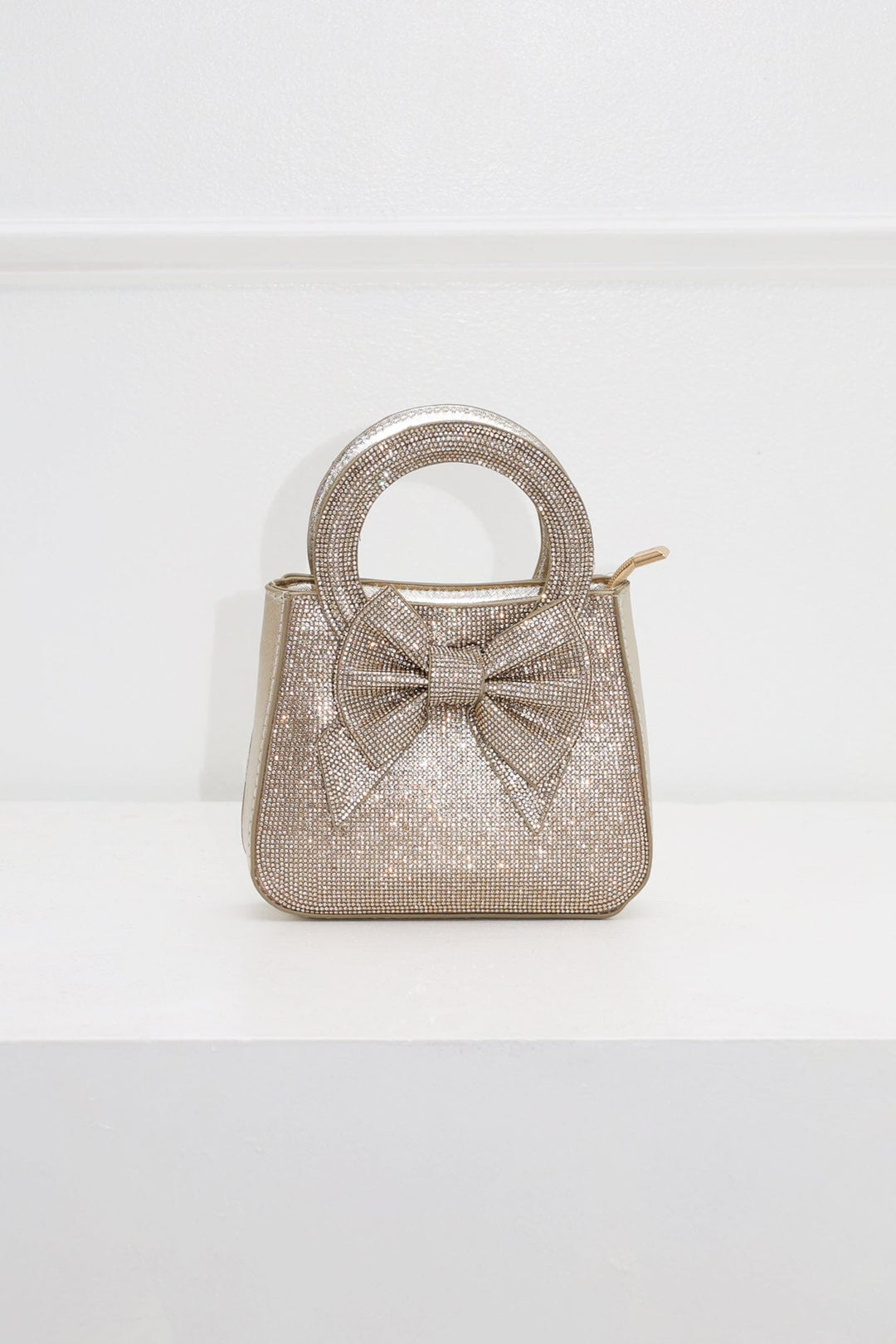 EDGE — gold rhinestone bow-embellished top-handle mini clutch, front view flat lay
