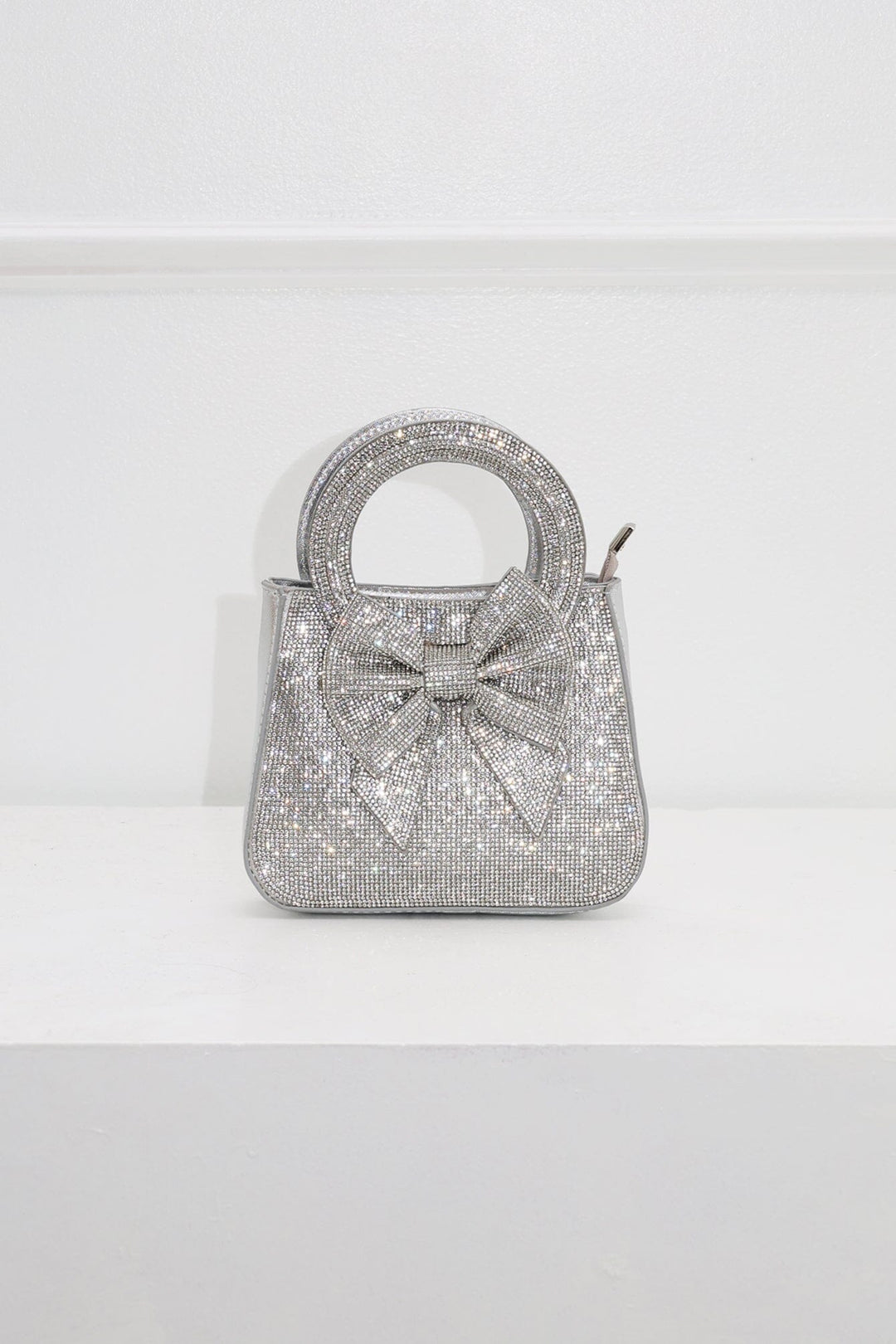 EDGE — silver rhinestone bow-embellished top-handle mini clutch, front view flat lay