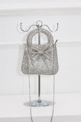 EDGE — silver rhinestone bow-embellished mini clutch with chain strap, styled on a display stand