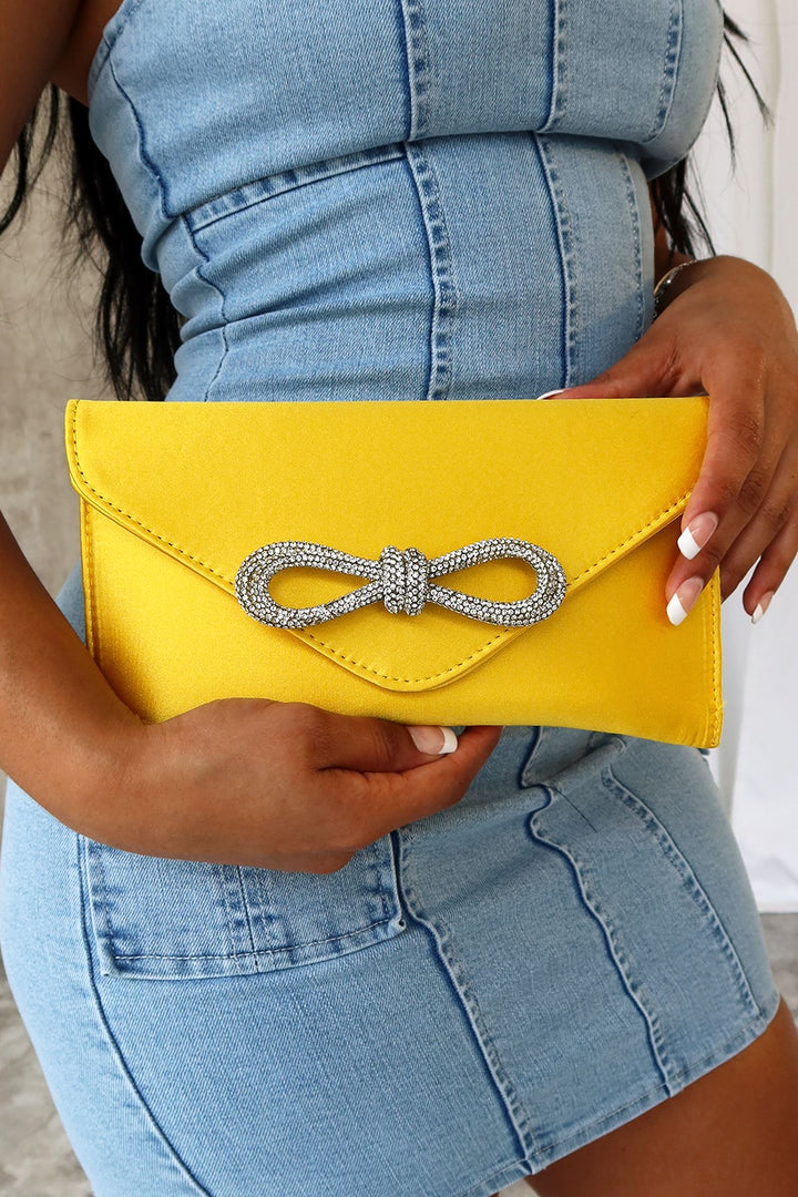 EDGE — yellow satin clutch with a crystal bow clasp, close-up held by a model